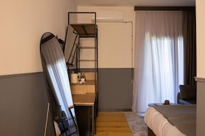 A compact room with a bunk bed, a desk with a chair, a small table, and a window with curtains.