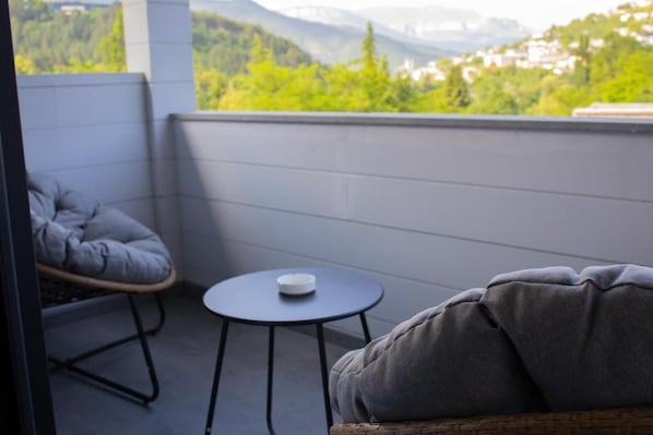 A balcony with a cushioned chair and a small table, overlooking a mountainous landscape.