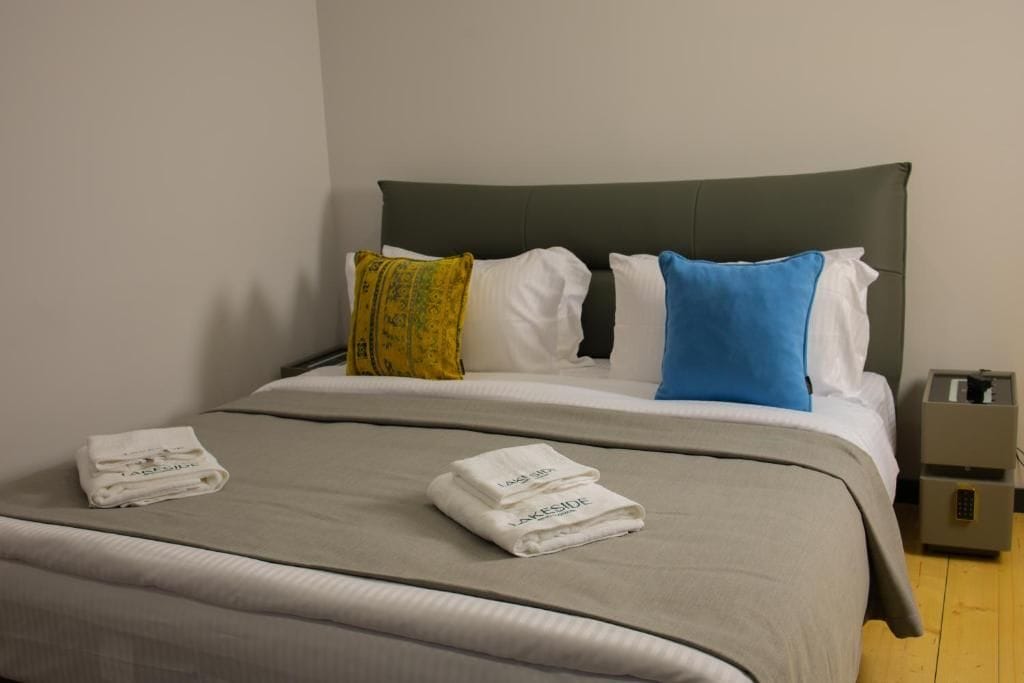 A neatly made bed with a grey headboard, white and blue pillows, and two folded towels on the bed.