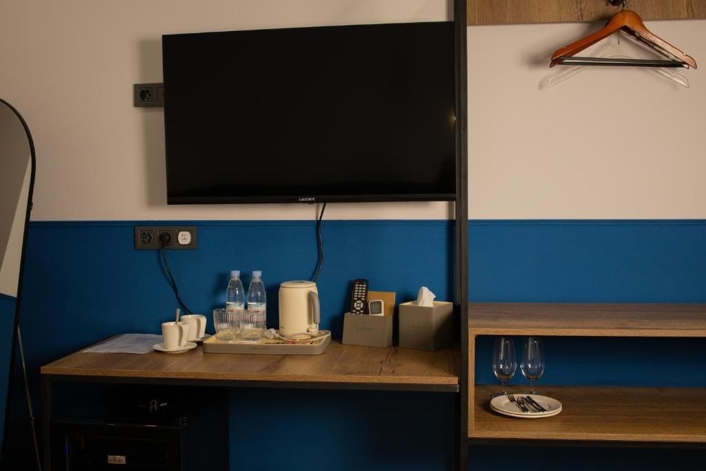 Habitación de hotel con televisor de pantalla plana montado en la pared, un escritorio de madera con una bandeja de objetos, un control remoto y una caja de pañuelos.