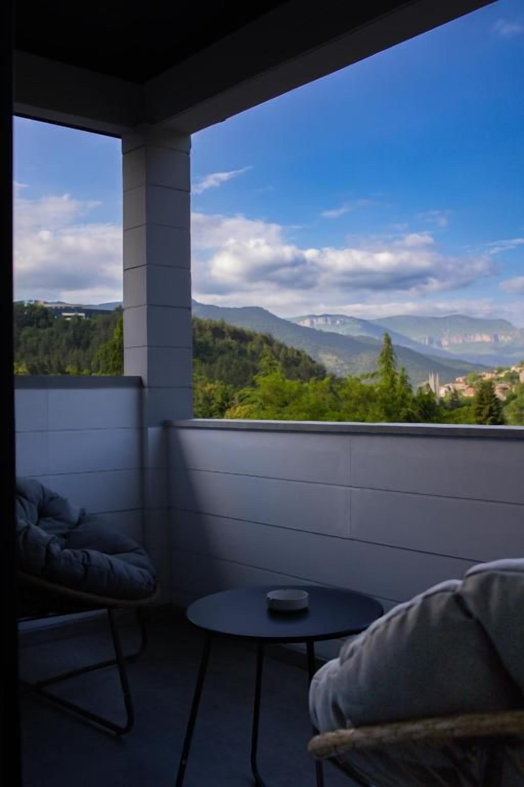 A balcony with a view of mountains and a table with a chair.
