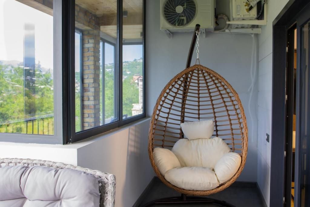 Una habitación con una silla colgante, un ventanal con vistas a zonas verdes y un equipo de aire acondicionado.