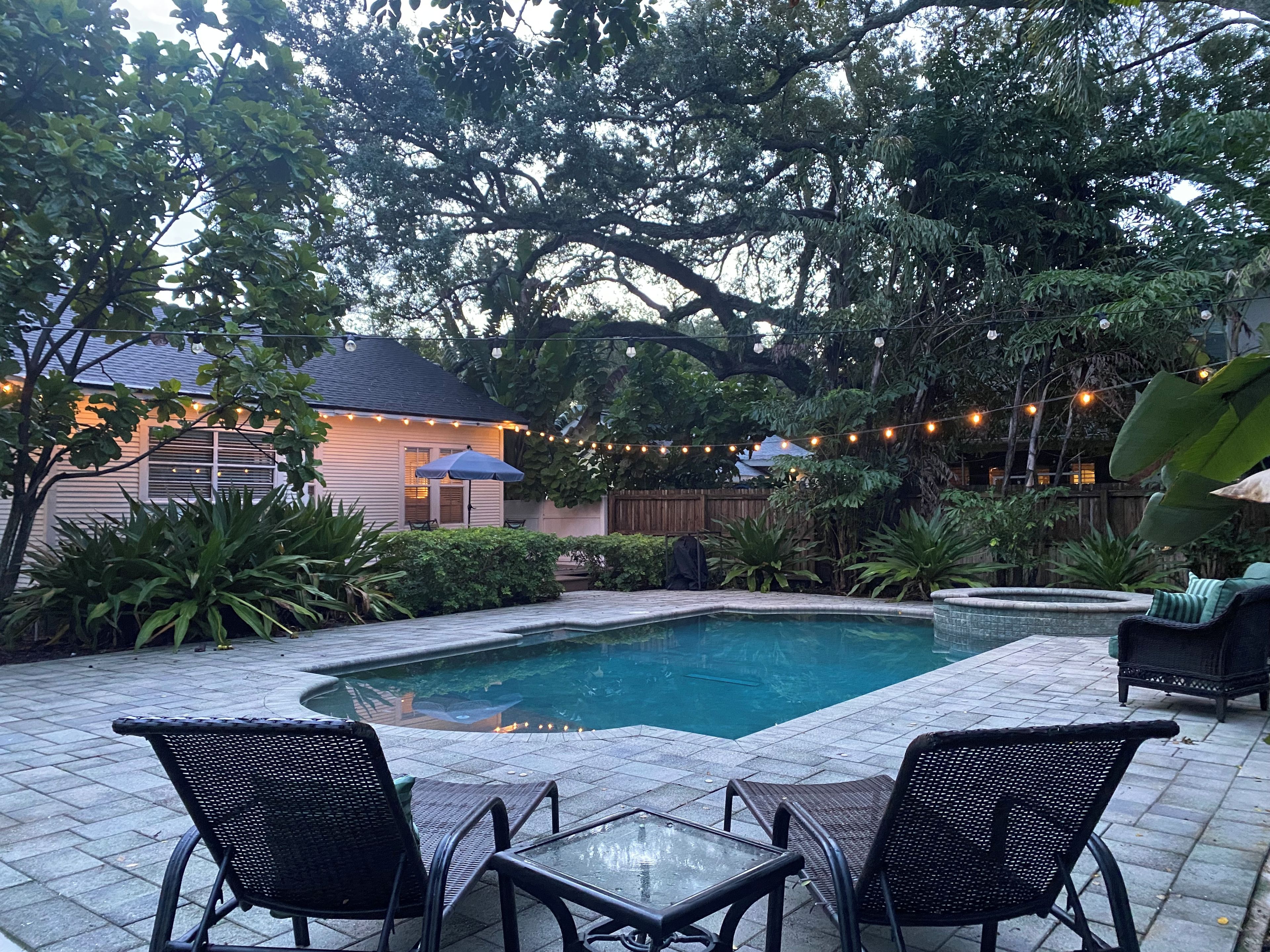 A backyard with a swimming pool, outdoor furniture, and string lights.