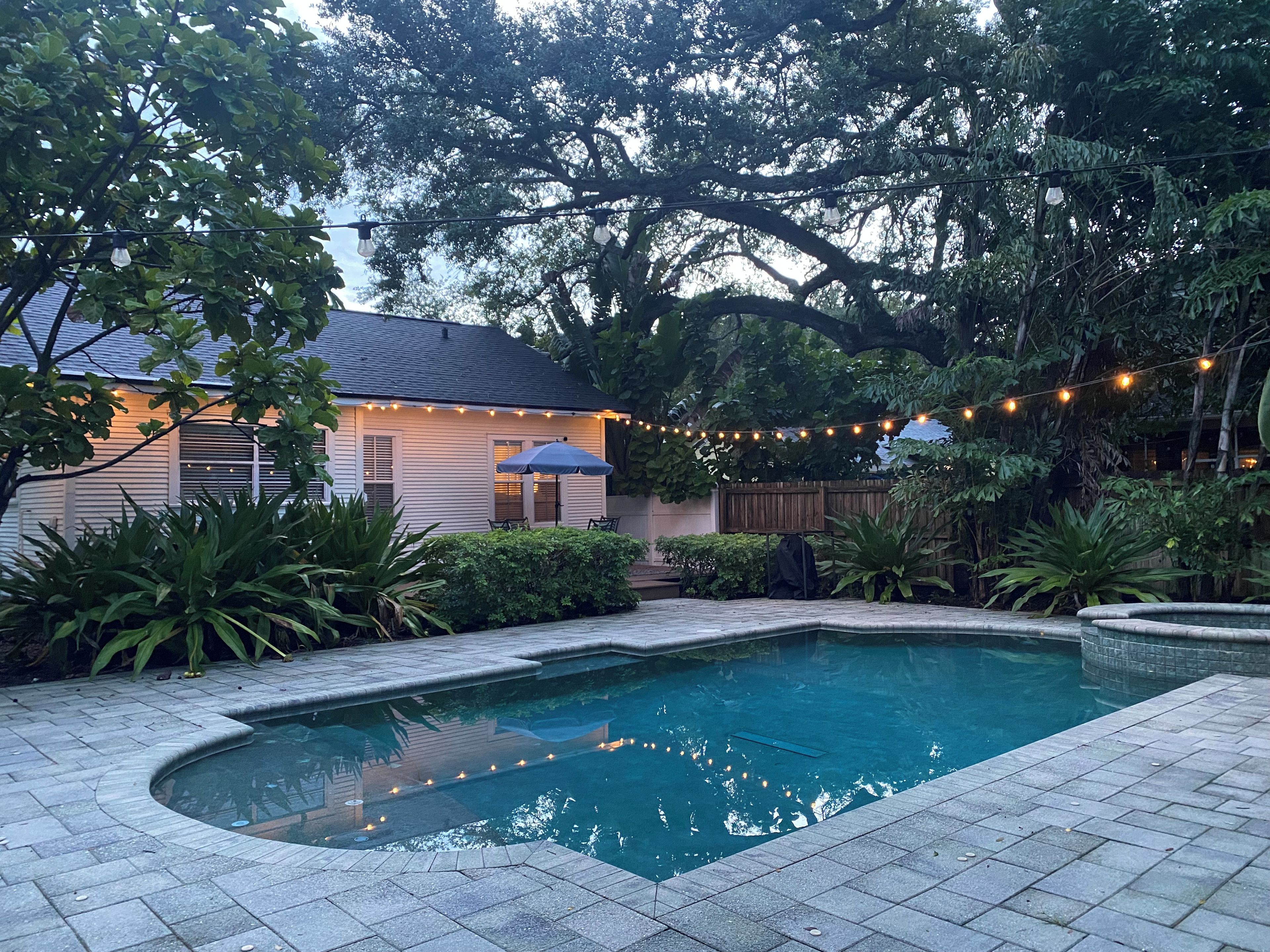 A backyard with a swimming pool, a covered patio, and string lights.