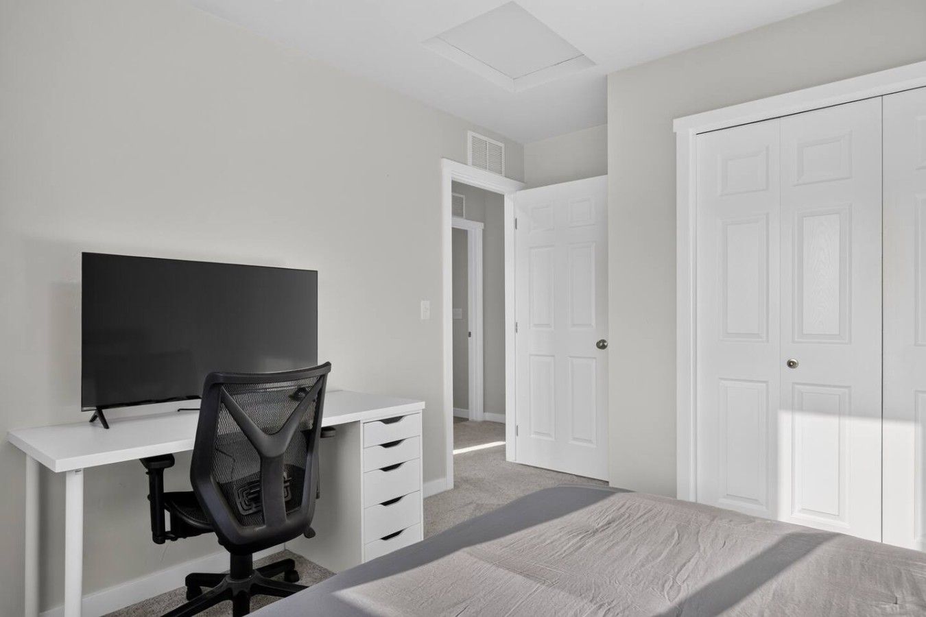 A bedroom with a bed, a desk with a chair, a television, and two white doors.