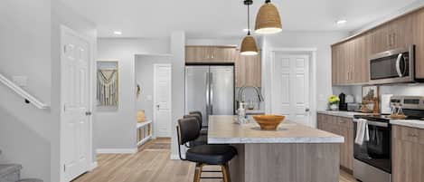 Una cocina moderna con una isla central, electrodomésticos de acero inoxidable y una lámpara colgante.