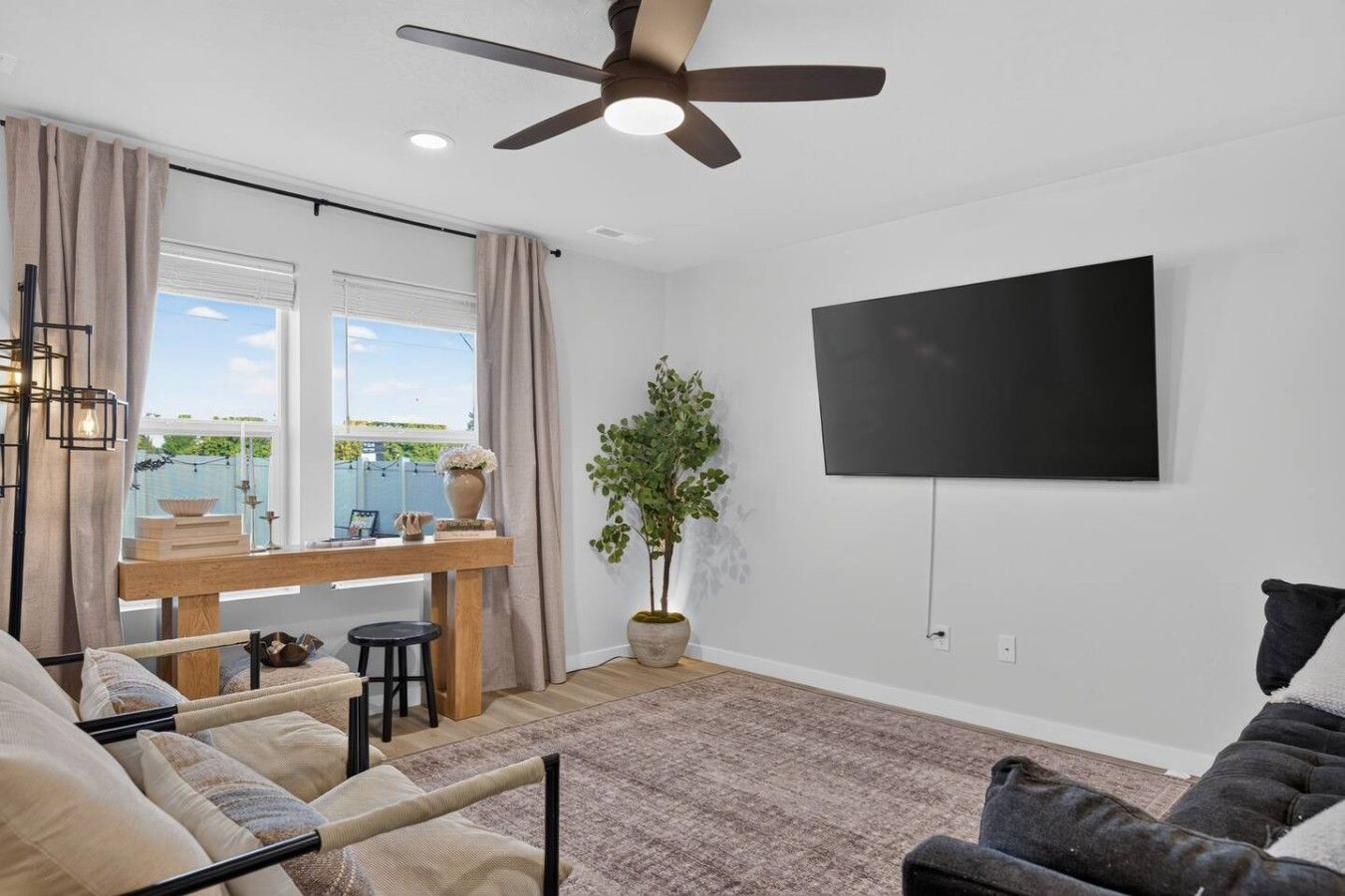 Ein modernes Wohnzimmer mit Deckenventilator, einem Wand-Flachbildfernseher, einem Essbereich mit Holztisch und einer großen Topfpflanze.