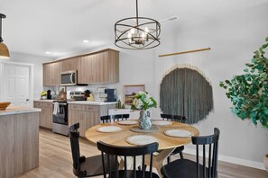 A modern kitchen with wooden cabinets, a central island, and a dining area with a round table and chairs. - Golden Sage Gathering House | Pet-Friendly 4BR Nampa Home • Sleeps 10 • Gym • Fenced Yard (Nampa)