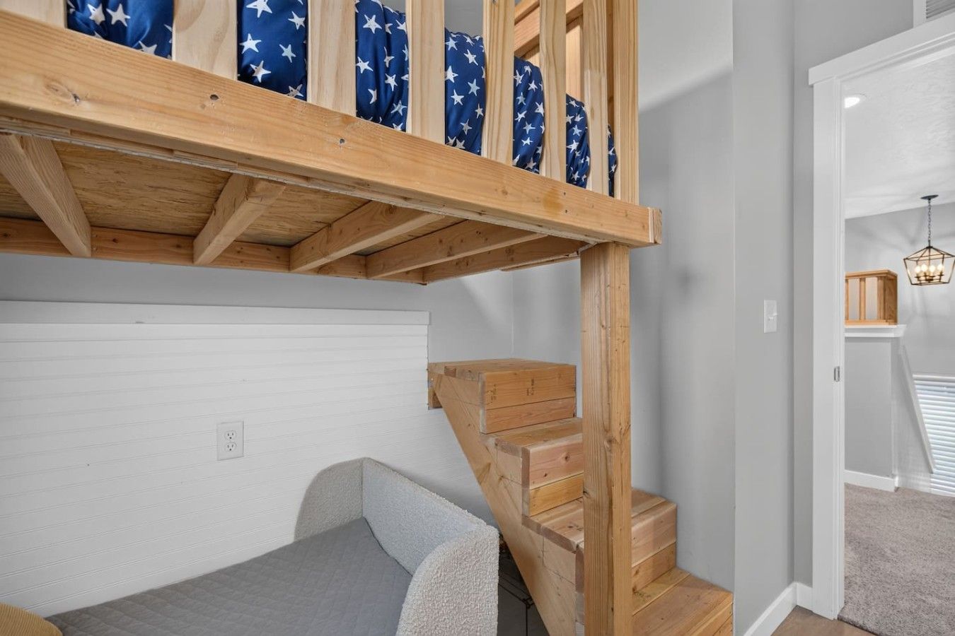 A loft bedroom with a wooden staircase, a bunk bed, and a small closet.