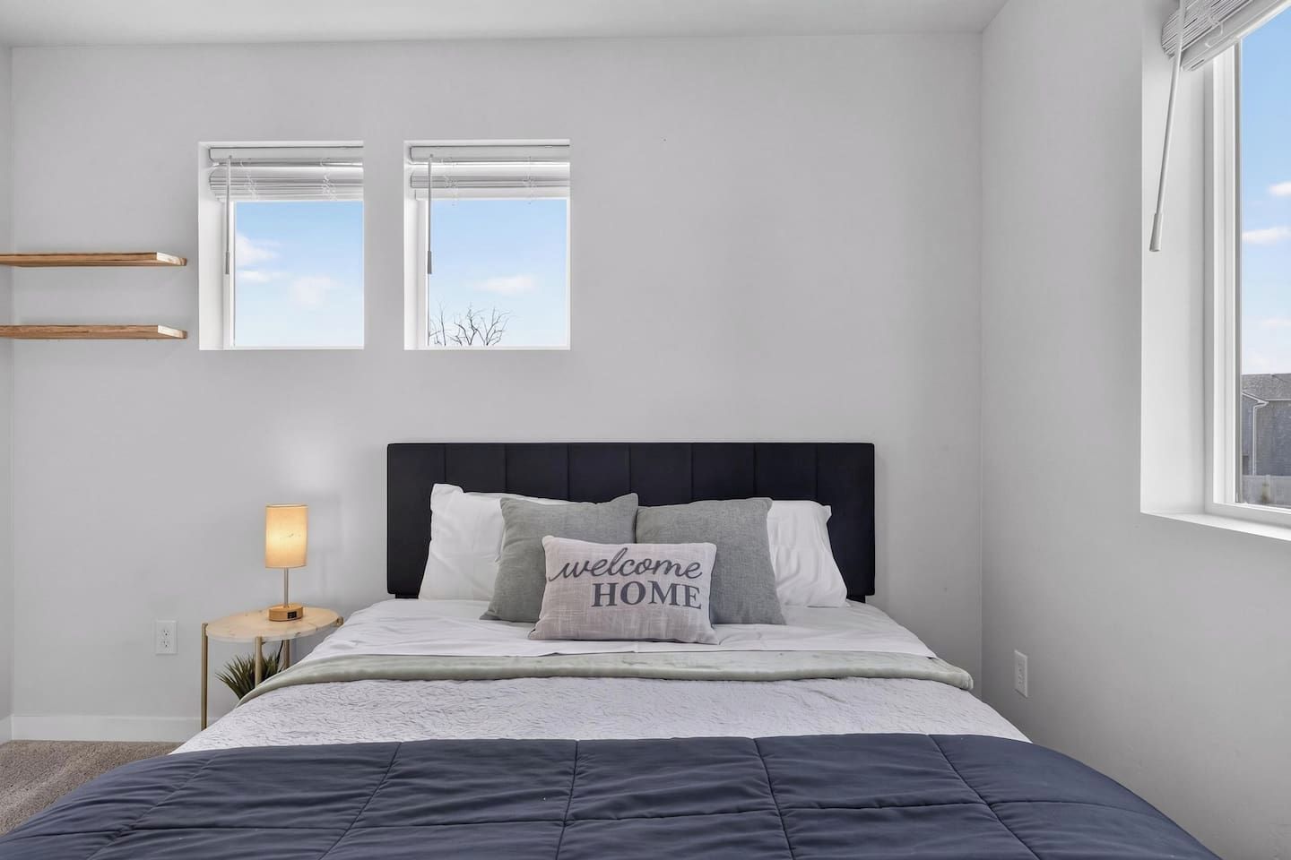 Een slaapkamer met een bed, een bedlampje, een raam en een wandplank.
