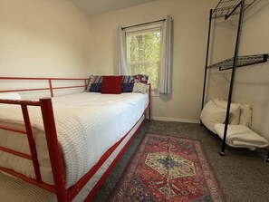 A single bed with a red frame, a window with blinds, a standing heater, and a patterned rug. - Morning Star Cottage (Star)