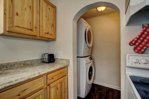 A laundry room with a washing machine, dryer, and oven. There is a wooden cabinet above the counter and a red and white checkered oven mitt hanging on the wall. - Morning Star Cottage (Star)
