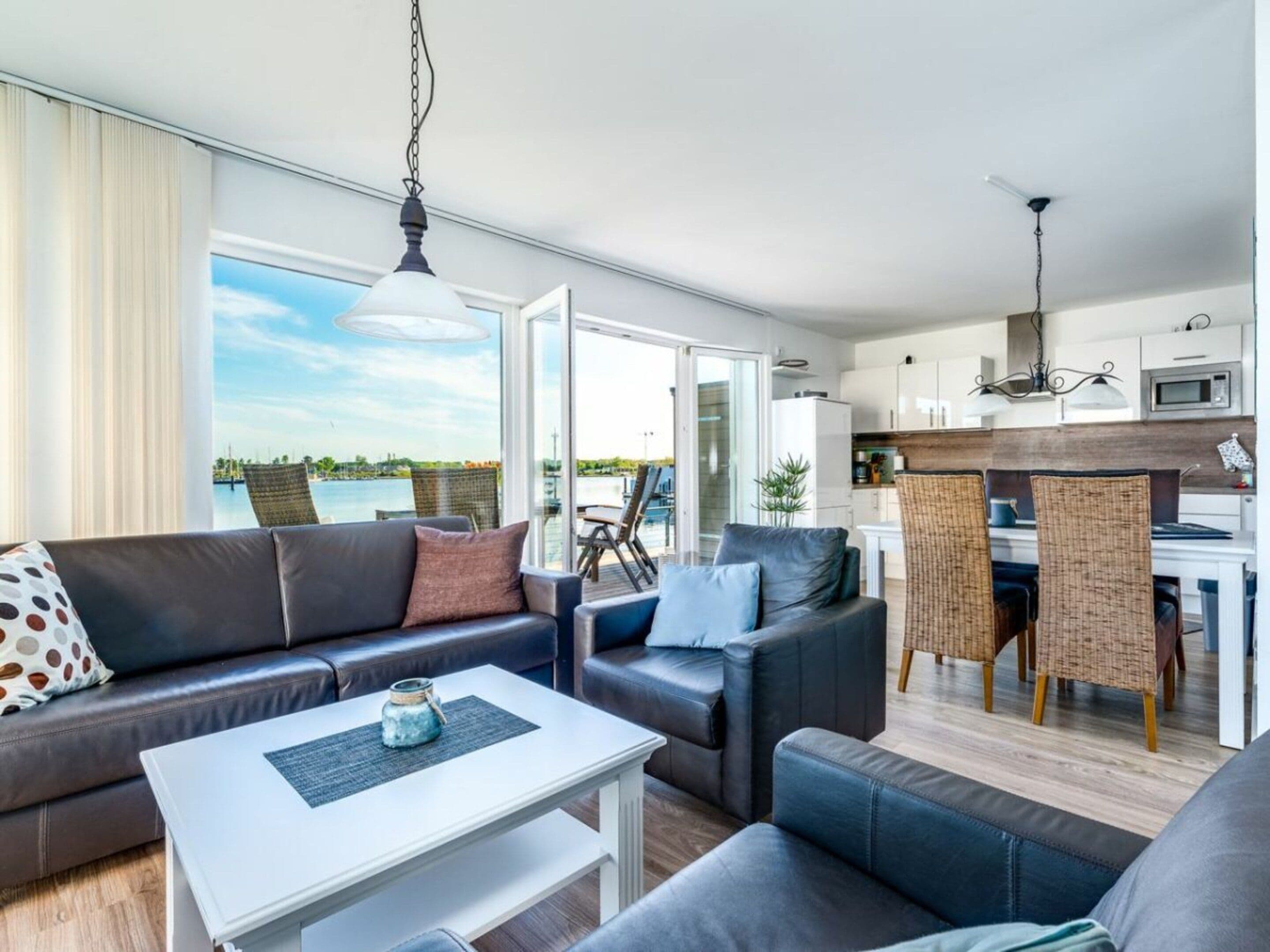 A modern living room with a sofa, chairs, a coffee table, and a view of a body of water through large windows.