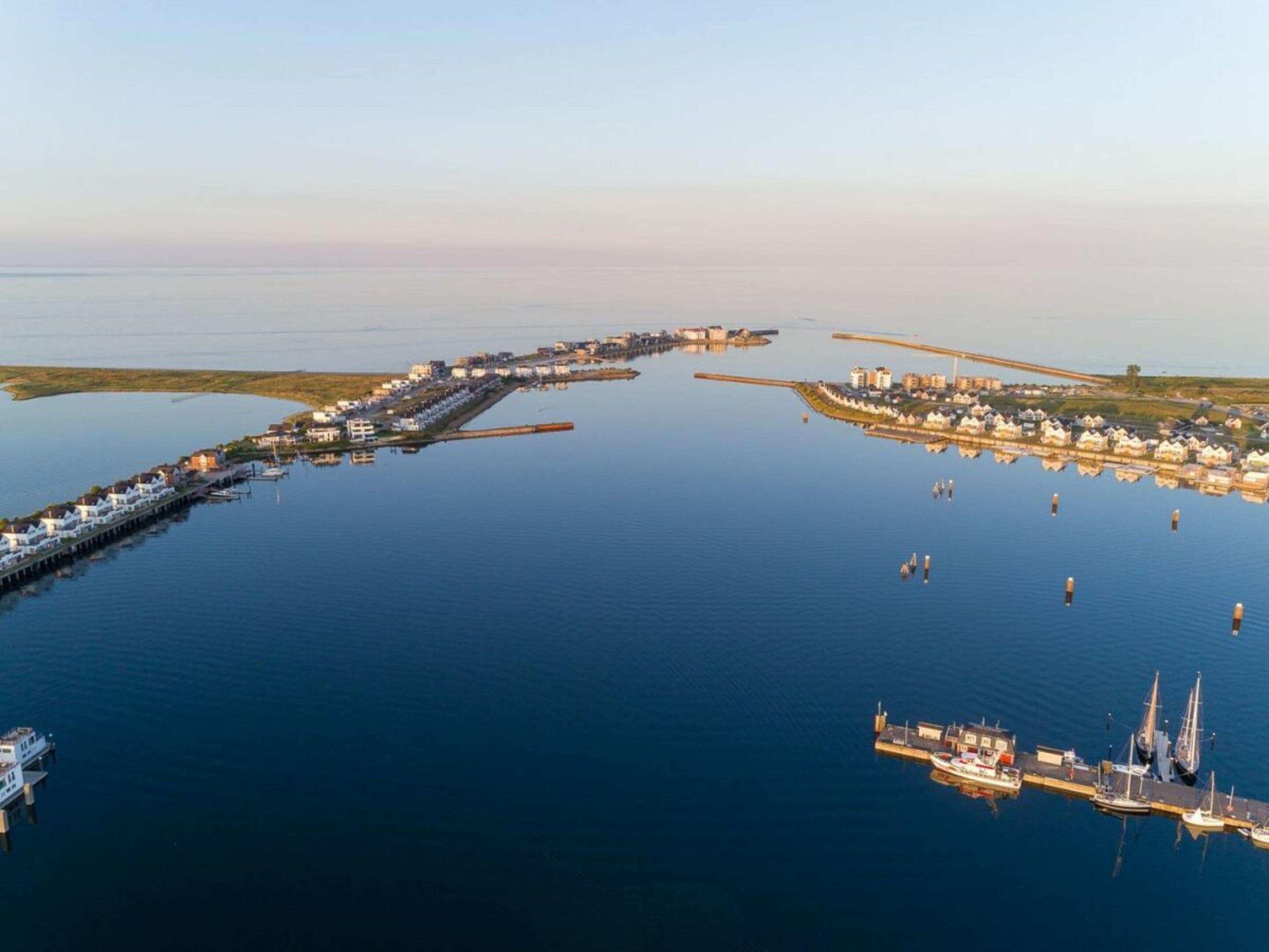 Vue aérienne d’une ville côtière avec un port de plaisance, des bâtiments situés au bord de l’eau et un pont.