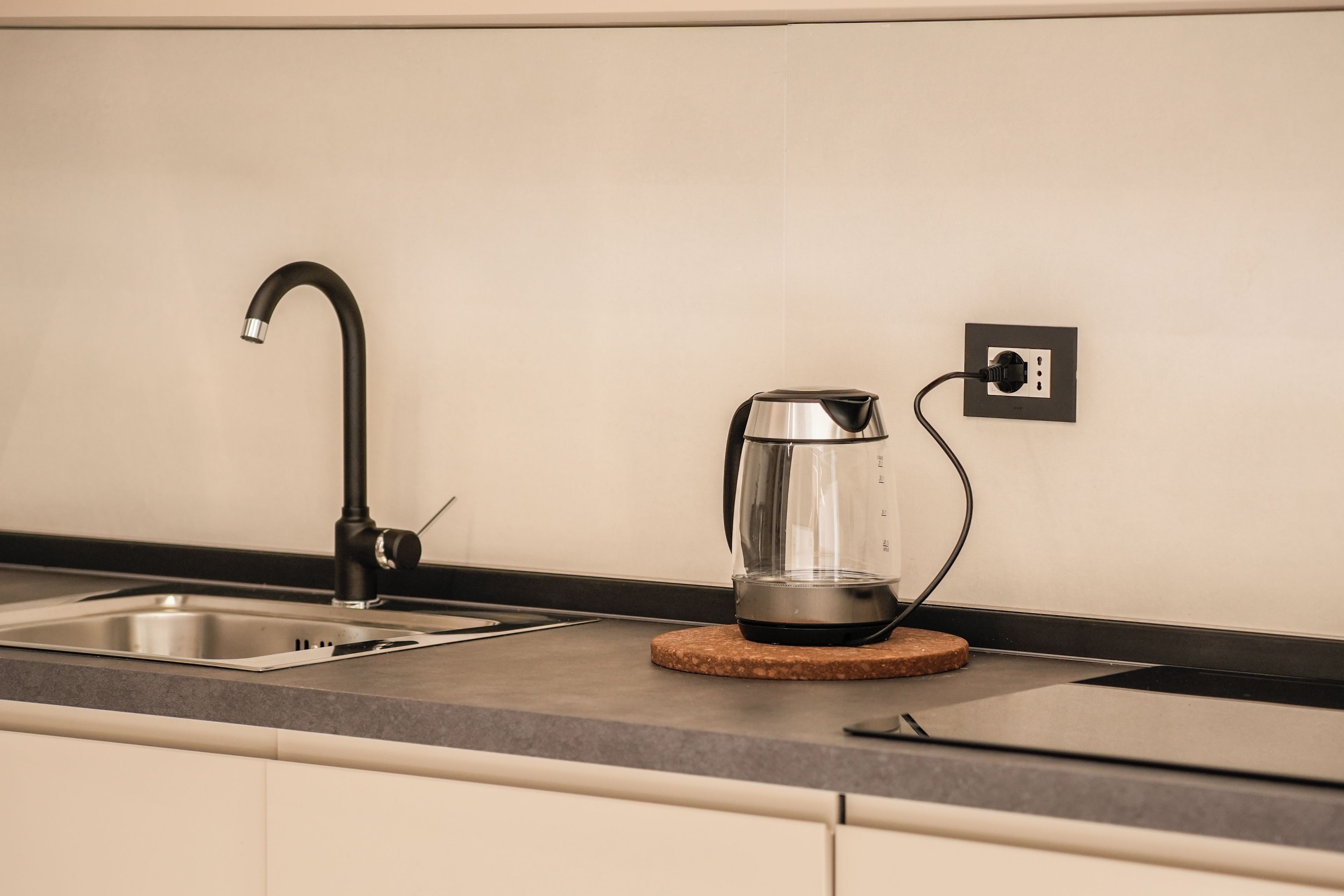 Una cucina con un lavello in acciaio inossidabile, un bollitore su un sottobicchiere e una presa elettrica sulla parete.