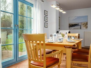 A dining area with a table set for four, chairs, a coffee station, and a view of the outdoors through a large window. - 11/t6 Holiday Home Park \"freesenbruch\" (Zingst)