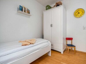 A bedroom with a single bed, a wardrobe, a small shelf with books, a clock, and a chair. - 11/t6 Holiday Home Park \"freesenbruch\" (Zingst)
