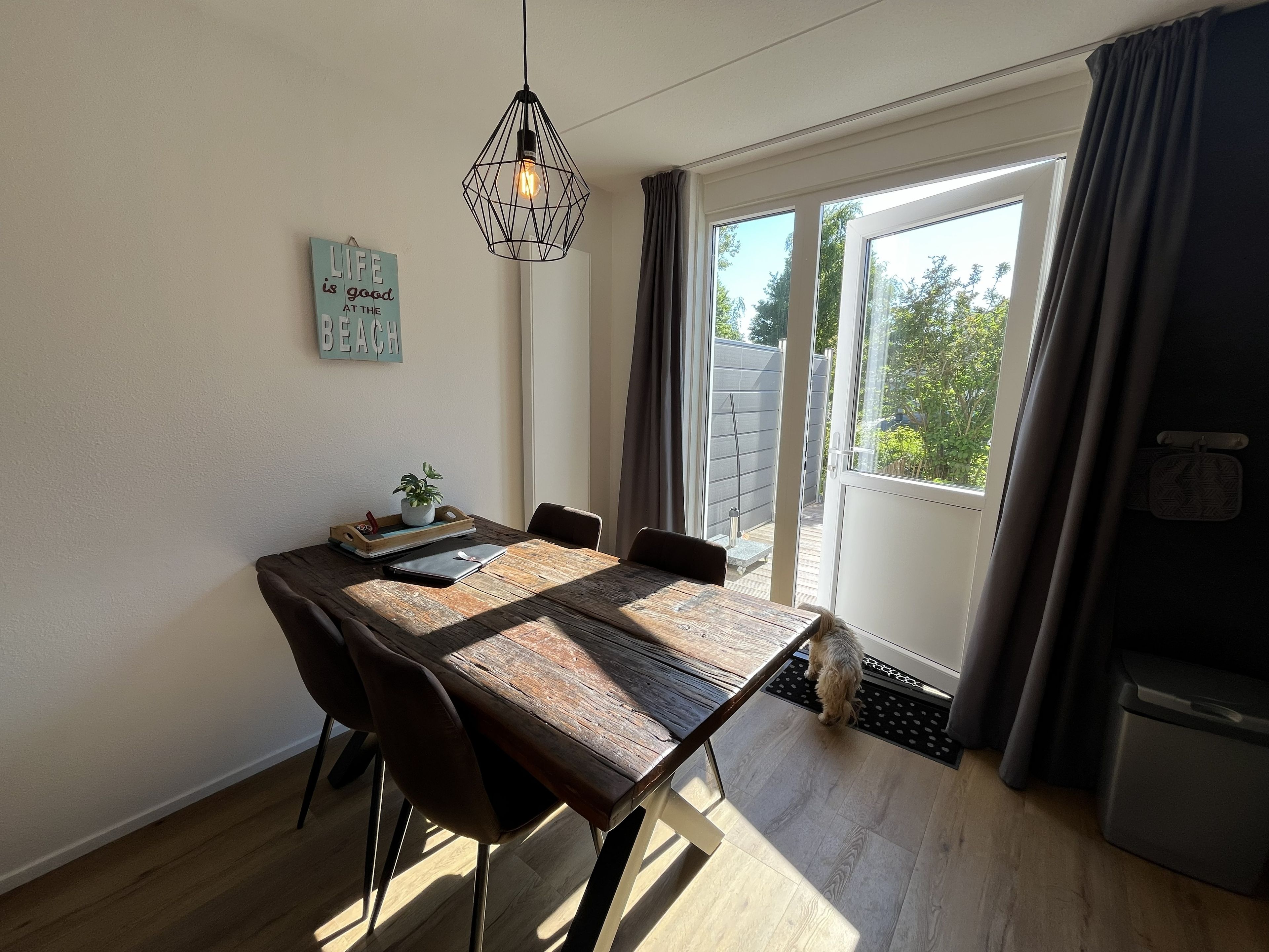 Ein Essbereich mit einem Holztisch, Stühlen, einer Hängelampe und Blick durch eine Glasschiebetür ins Freie.