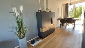 A modern living room with a dining area, a large potted plant, and a pet feeding station.