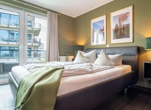 Ein Hotelzimmer mit einem Bett, zwei Nachttischen, einem Fenster mit Vorhängen und zwei gerahmten Bildern an der Wand.