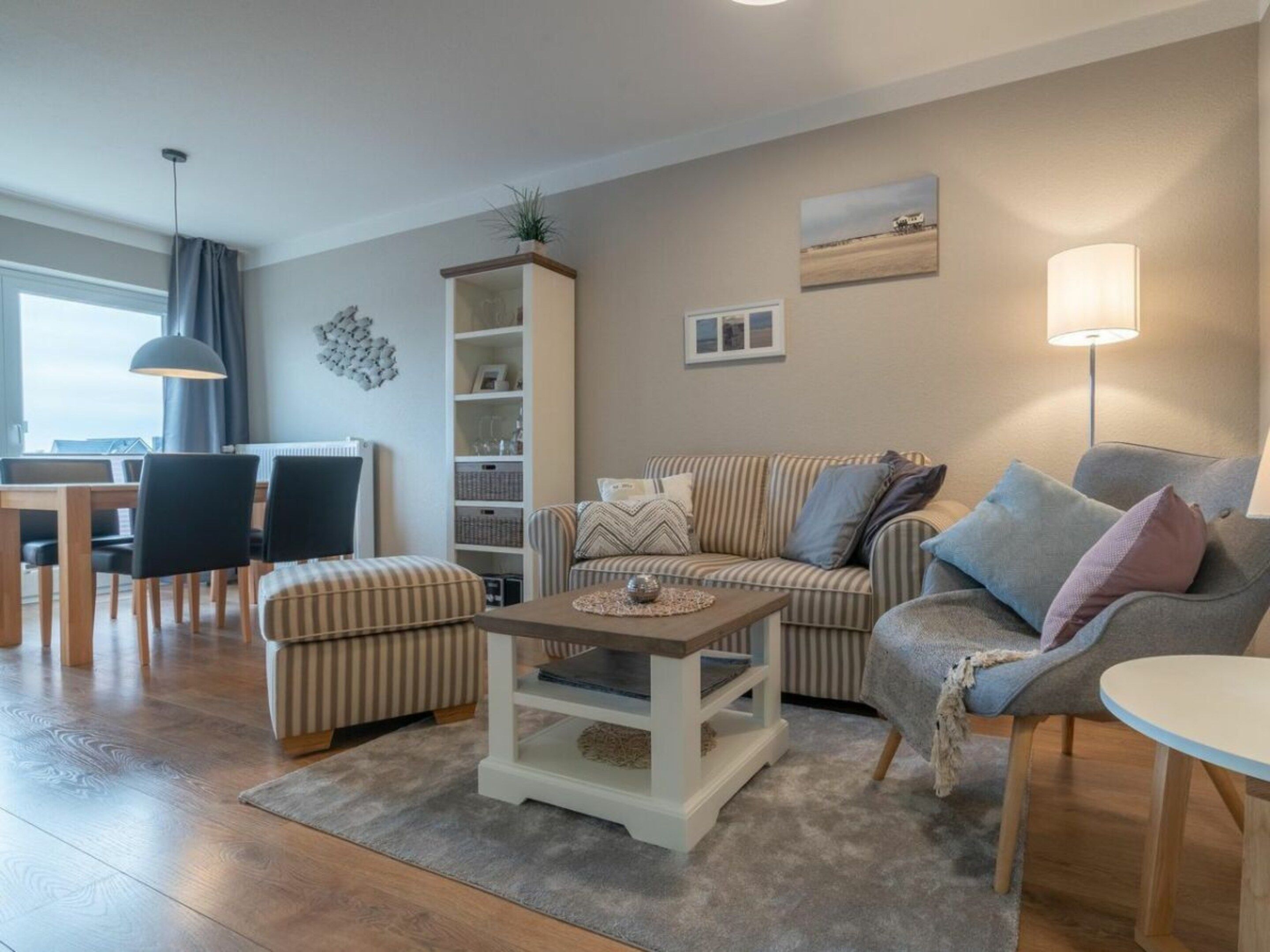 A living room with a striped sofa, a grey armchair, a coffee table, and a bookshelf.