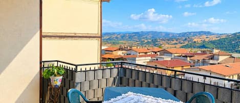 Un balcon avec une table et des chaises, un pot de fleurs et une vue sur la ville et les collines.