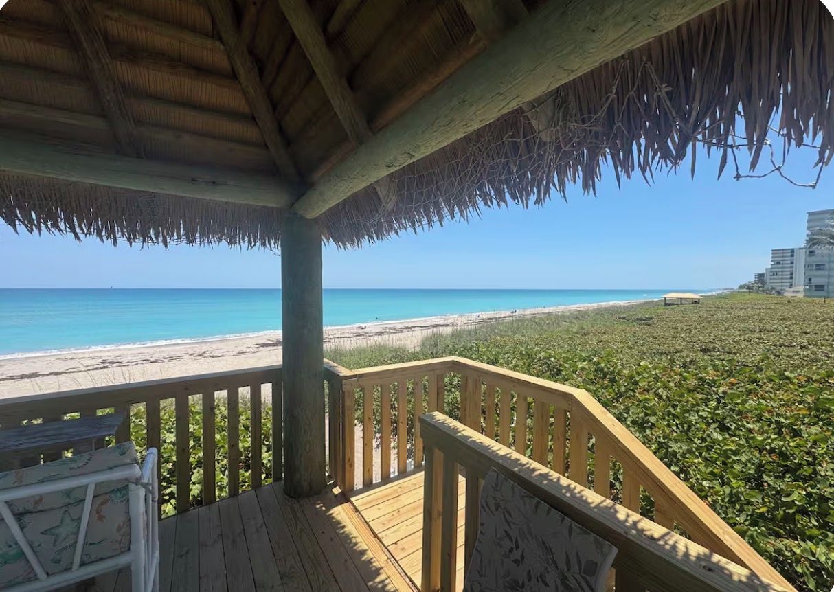 A wooden deck with a thatched roof overlooking a beach.