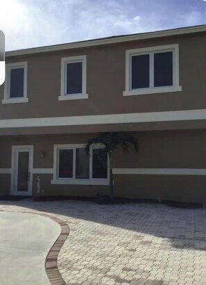 A two-story building with a flat roof, a paved driveway, and a small tree in the front yard. - Island Retreat with Private Beach, River Views, Great Restaurants & Live Music (Jensen Beach)