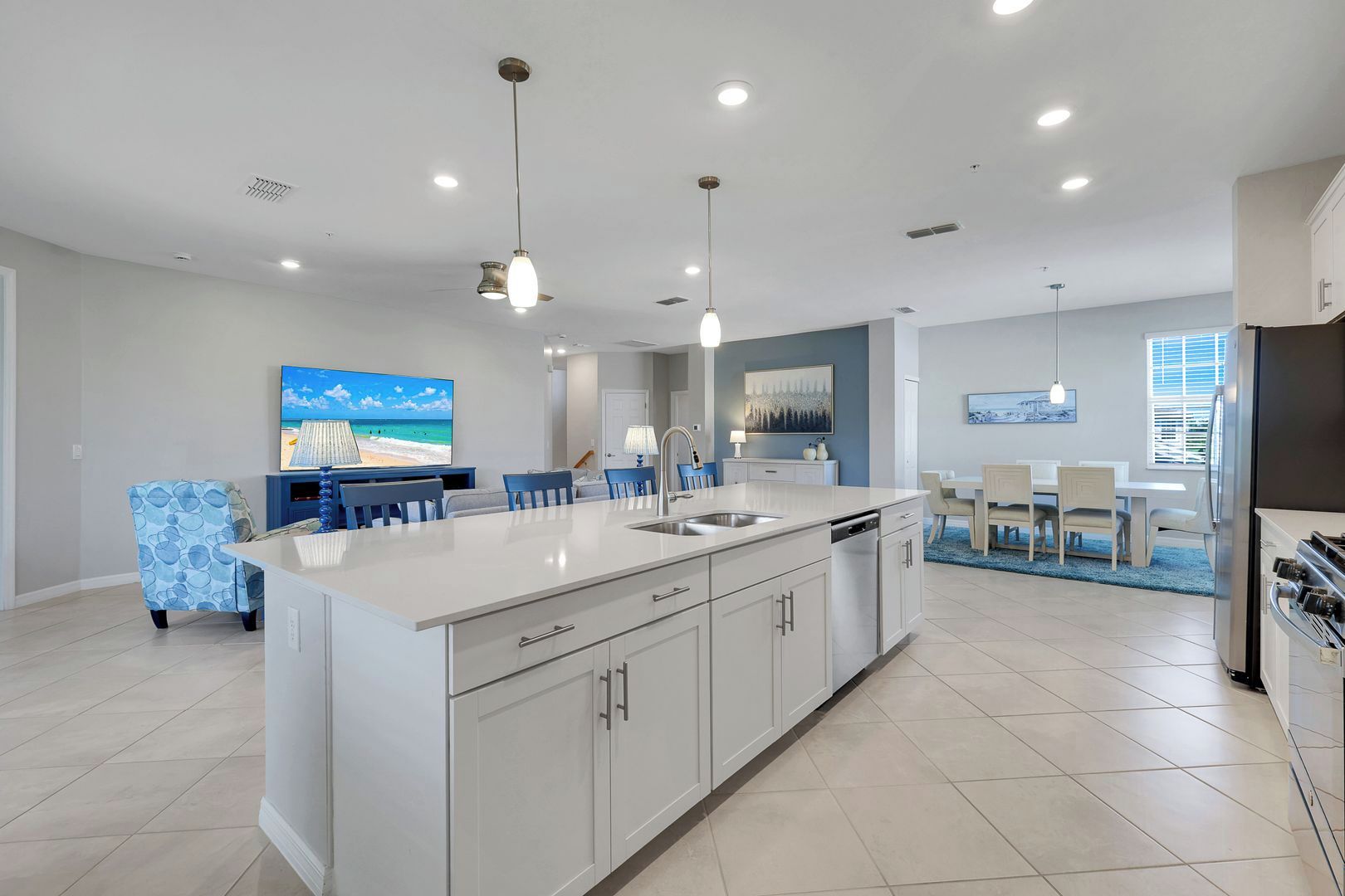 A modern kitchen with a central island, overhead pendant lighting, and a dining area with a view of the beach.