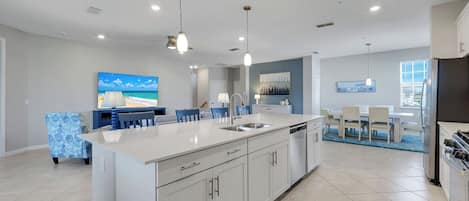 A modern kitchen with a central island, overhead pendant lighting, and a dining area with a view of the beach.