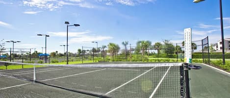 A tennis court with a net, surrounded by a fence, and street lamps.