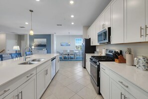 A modern kitchen with white cabinetry, a central island, stainless steel appliances, and a dining area with a blue chair. - Michigander's Dream (Punta Gorda)
