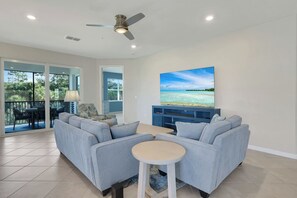 A modern living room with a sectional sofa, a small round table, and a flat-screen TV mounted on the wall. - Michigander's Dream (Punta Gorda)