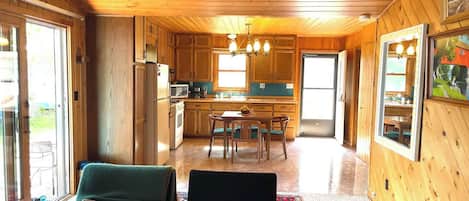 A wooden interior with a kitchen, dining area, and two lounge chairs.