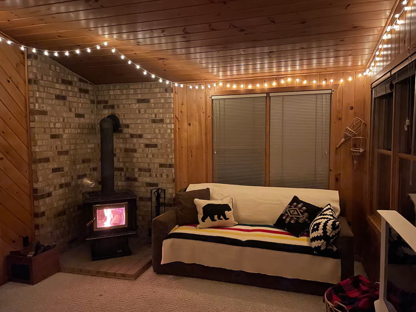 Et hyggeligt rum med murstensvæg, træloft, sofa med mønstrede puder og pejs med TV.