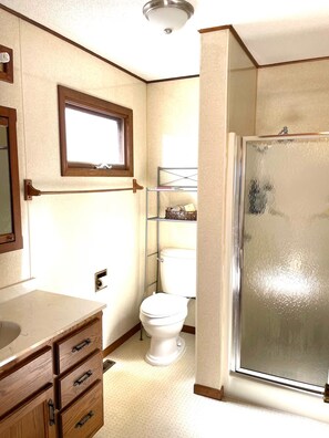 Ein Badezimmer mit Toilette, einem Holzschrank, einem Ablagebereich für Toilettenartikel und einer Duschkabine.