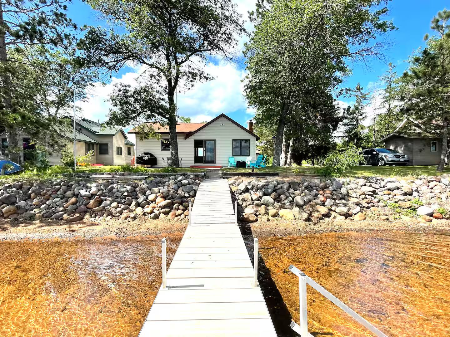 A wooden dock leading to a house with a stone wall and a clear view of the surrounding area.