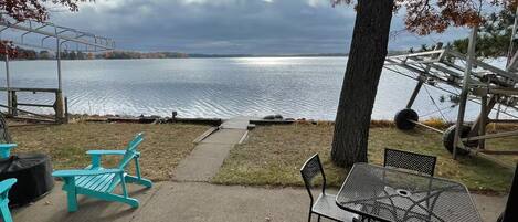 A lakeside seating area with a metal table and chairs, a wooden bench, and a view of the lake.