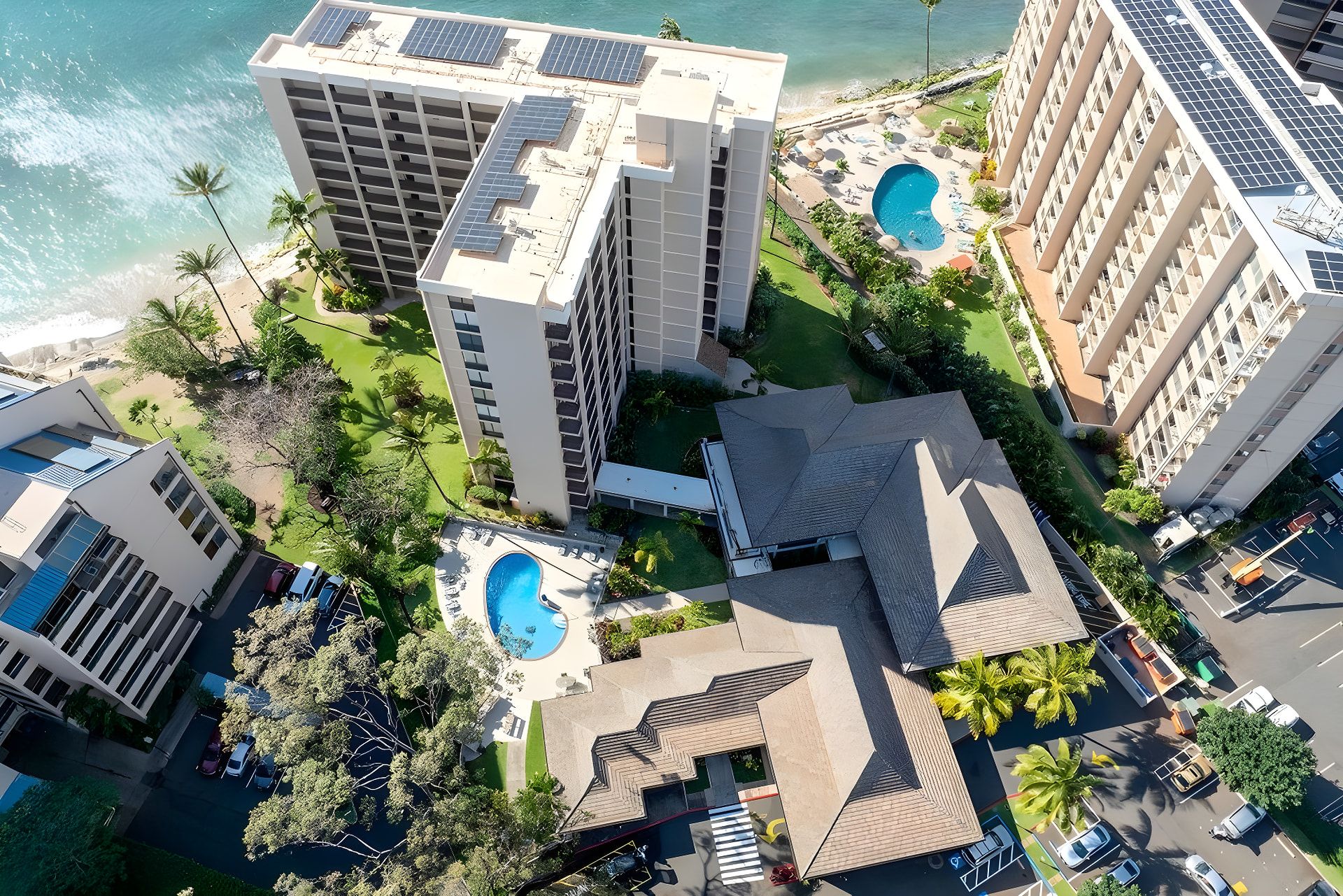 Ein Hochhaus-Hotel mit mehreren Schwimmbecken, Blick auf den Strand und einem Parkplatz.
