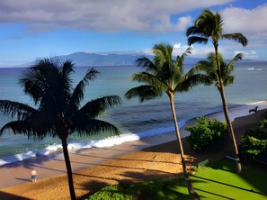 A beach with palm trees, ocean waves, and a distant mountain. - Kahana, Valley Isle Resort, Spacious 4 BR, Beachfront, Sleeps 12 (Lahaina)
