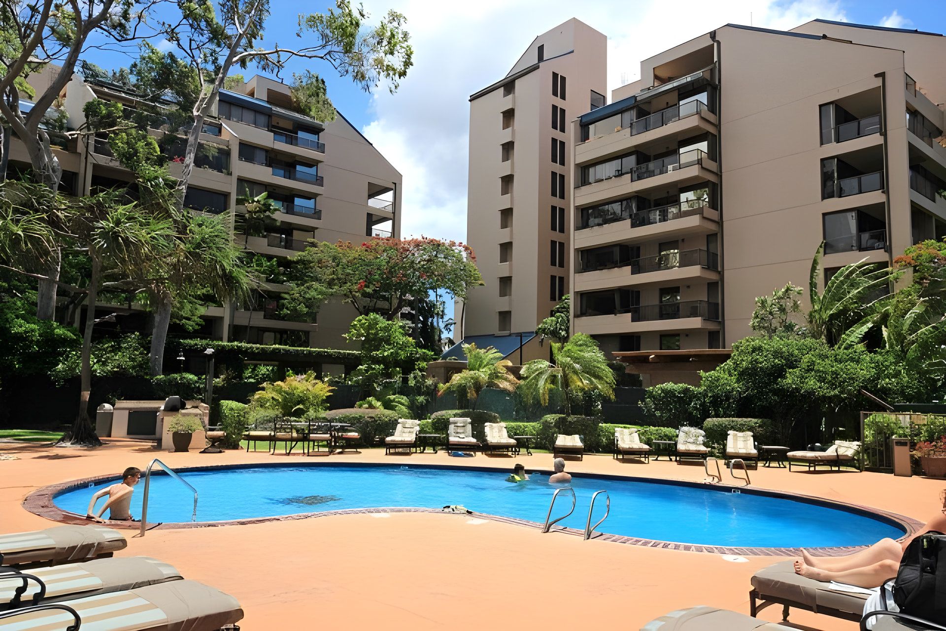 Une piscine entourée de chaises longues et un immeuble à plusieurs étages doté de balcons.