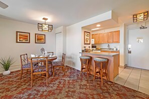 A modern kitchen with wooden cabinets, a bar area with stools, and a dining table with chairs. - Kahana, Valley Isle Resort, Spacious 4 BR, Beachfront, Sleeps 12 (Lahaina)
