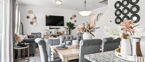 A modern dining area with a wooden table, grey upholstered chairs, and a marble countertop.