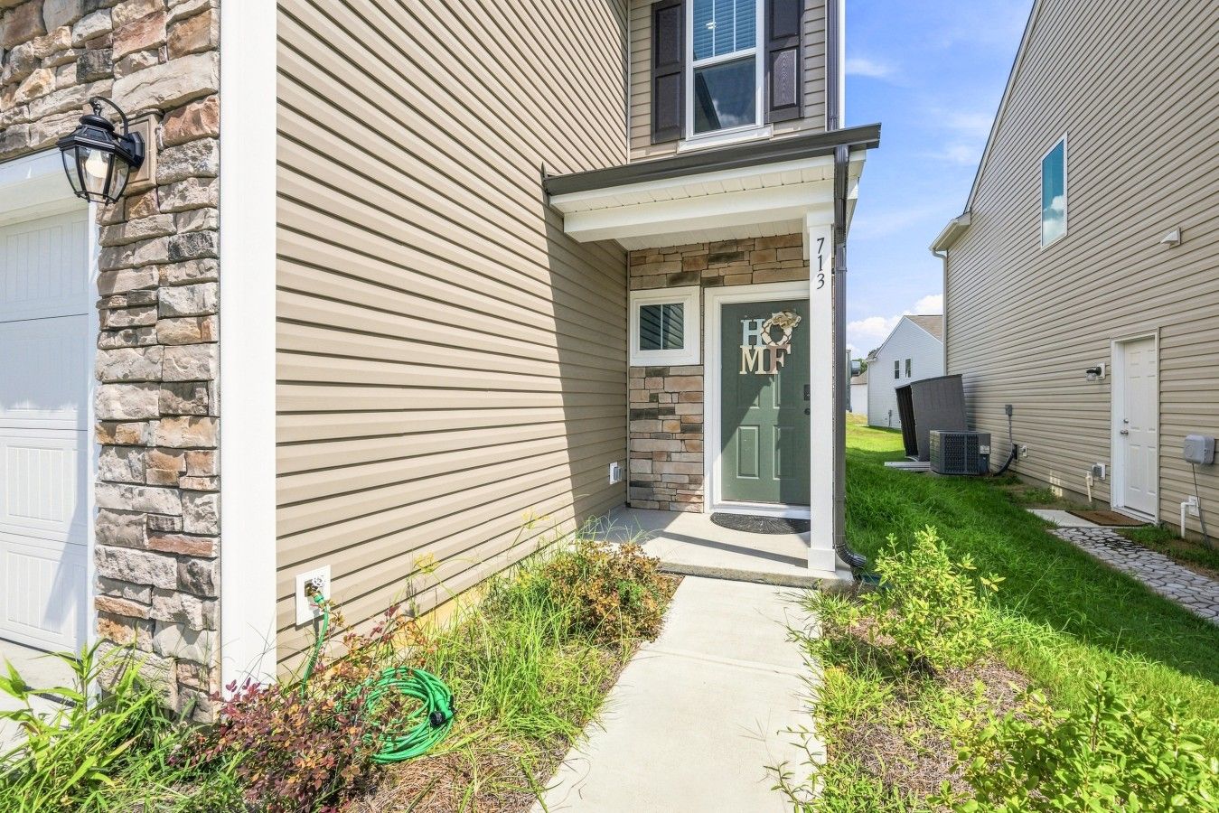 A residential house with a stone facade, a front door with a nameplate, and a visible air conditioning unit.