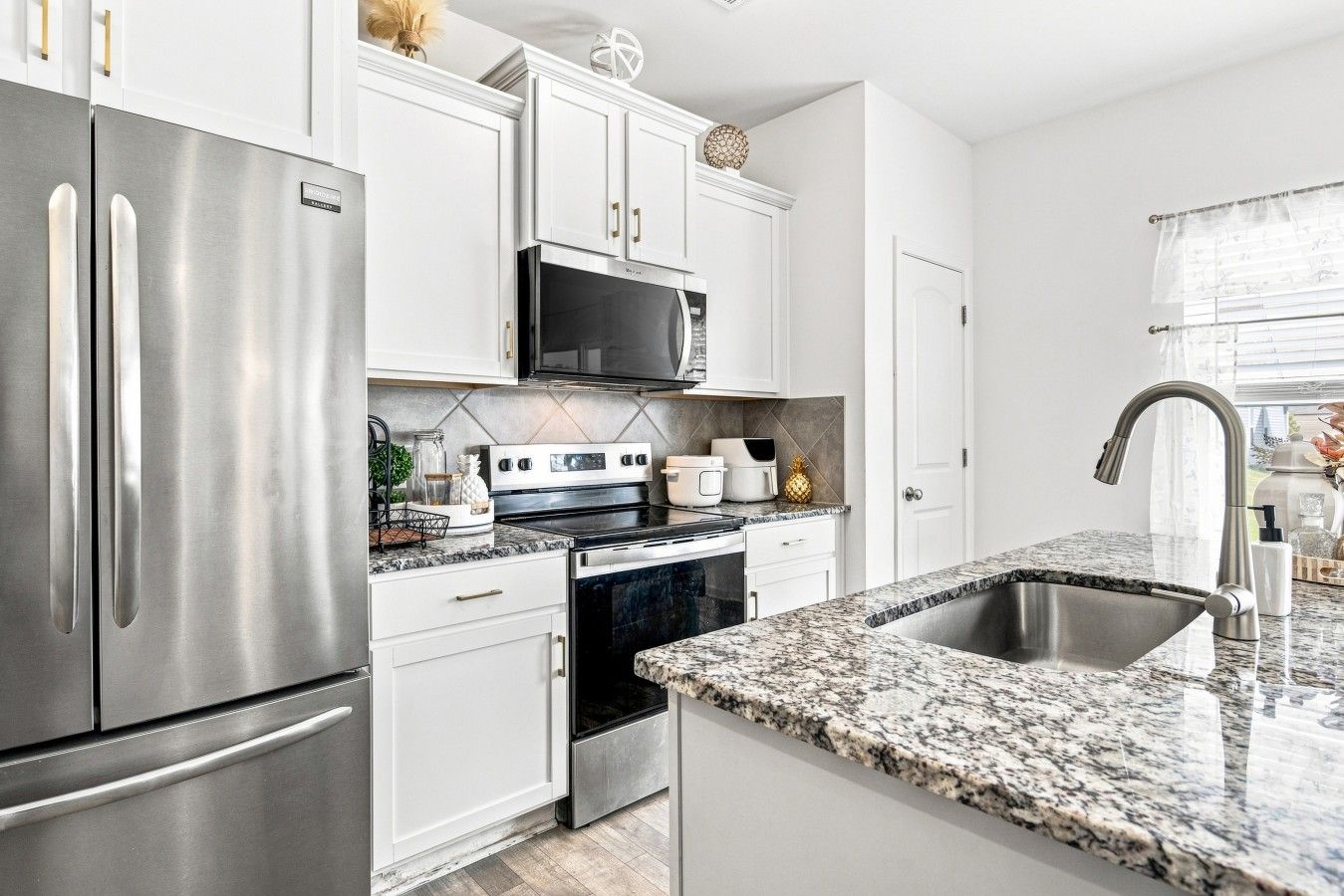A modern kitchen with stainless steel appliances, white cabinetry, and a granite countertop.