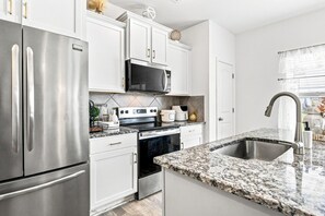 A modern kitchen with stainless steel appliances, white cabinetry, and a granite countertop.
