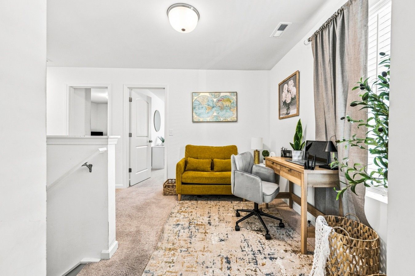 A hallway leading to a living room with a mustard sofa, a grey armchair, a wooden desk, and a map artwork on the wall.