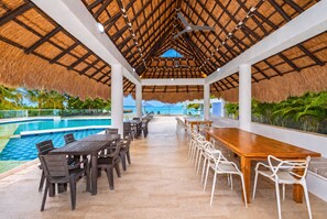 An indoor pool area with a thatched roof, wooden tables, and chairs, overlooking a clear blue pool. - CASA PRIVADA 4 - AREIA BARU (Bolívar)