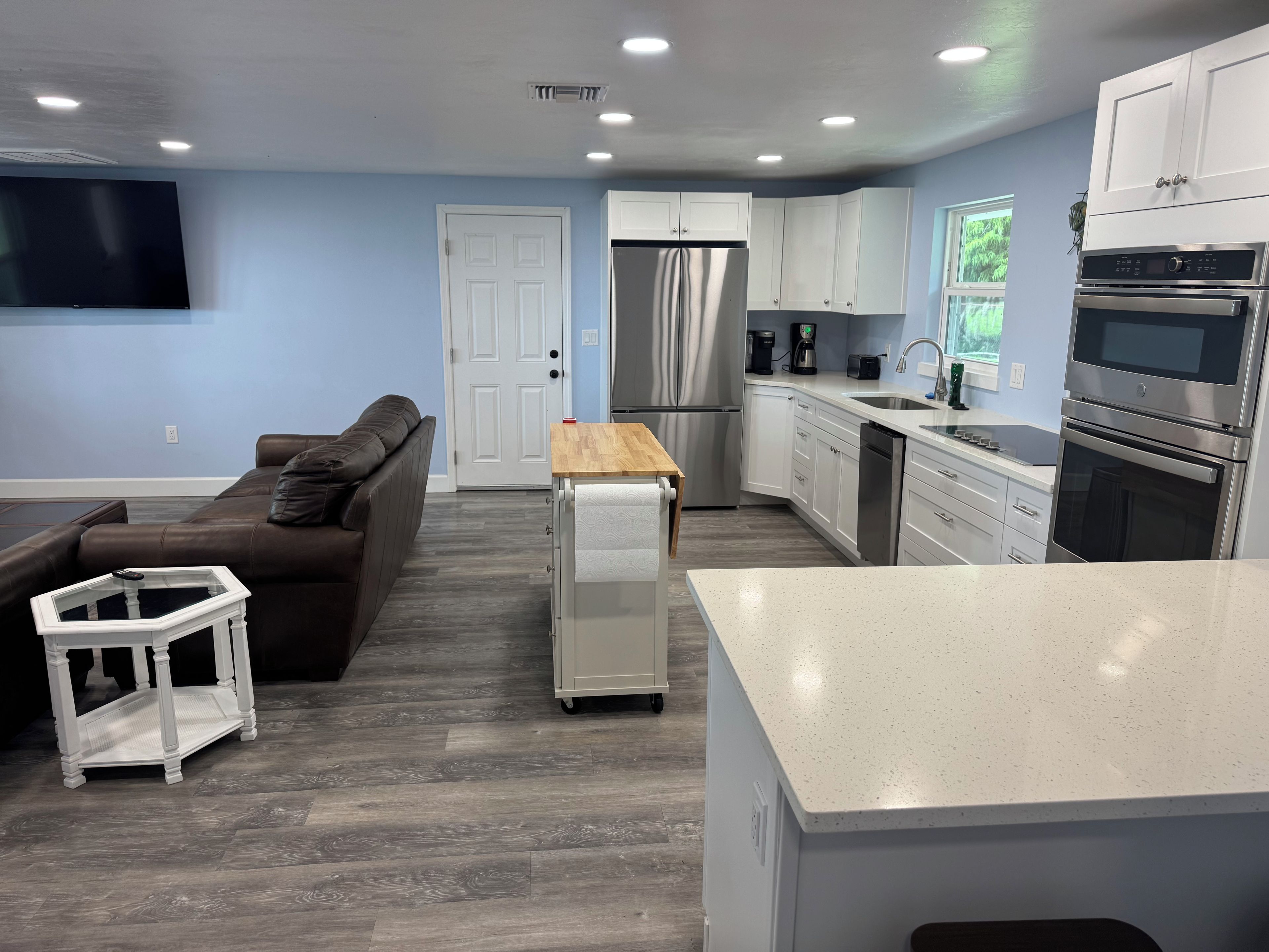 A modern kitchen with white cabinetry, stainless steel appliances, and a wooden dining table.