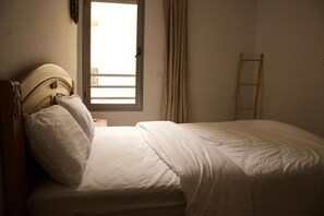 Una cama individual con cabecera de madera, una mesita de noche y una ventana con cortinas.